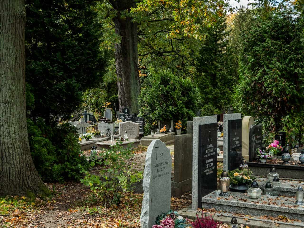 Peaceful cemetery with headstones surrounded by green trees and flowers.