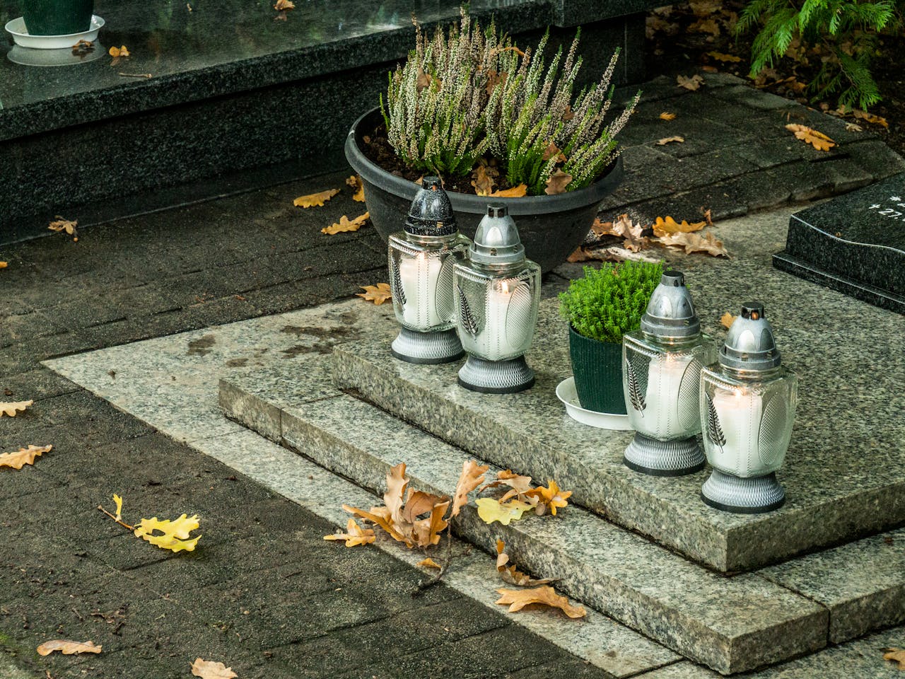 Peaceful cemetery scene with candles and autumn leaves on gravestone.