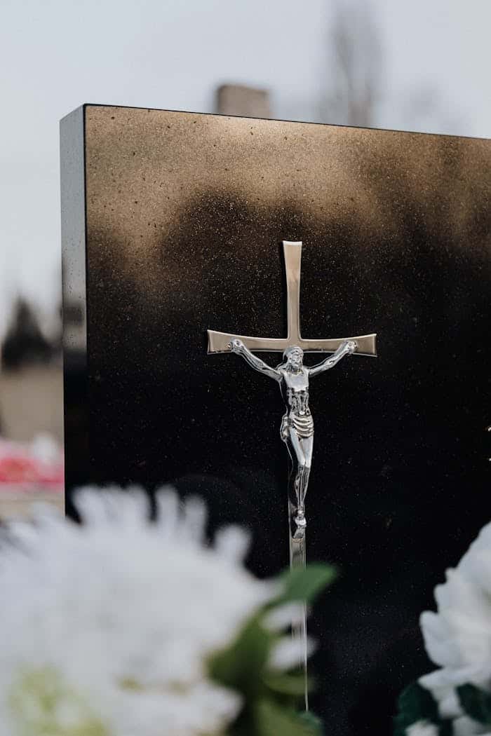 A detailed silver crucifix on a reflective black background with soft floral foreground.