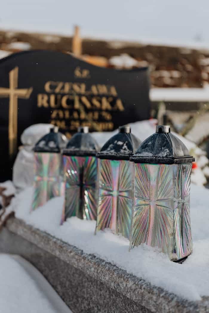 Snowy cemetery scene with glass lanterns on a gravestone during winter.